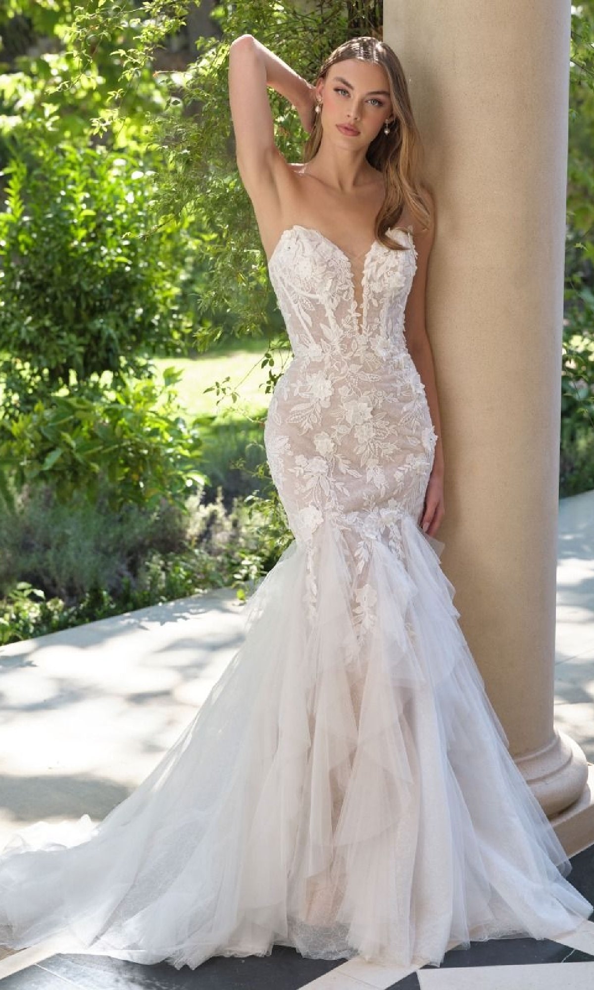 Woman in a white mermaid wedding dress standing outdoors with greenery in the background